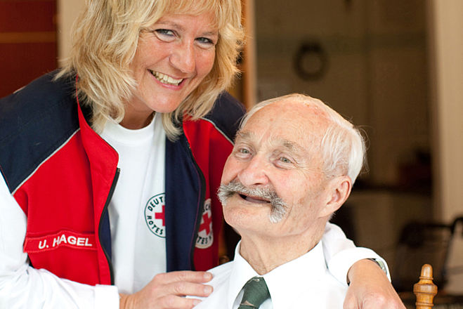 Ein lachender Senior mit einer DRK Mitarbeiterin. 